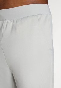 Hellgraue Sporthosen mit einem breiten elastischen Bund, Seitentasche und glatter Textur, die für Komfort und Bewegungsfreiheit ausgelegt sind.