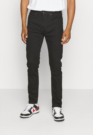 Vaqueros de denim negro con un corte ajustado y un diseño clásico de cinco bolsillos, combinados con zapatillas blancas y negras con acentos rojos.