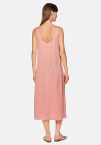 Rosa, ärmelloses Maxikleid mit tiefem Rückenausschnitt, glattem Stoff, knöchellangem Schnitt und einfachem Design. Getragen mit flachen Sandalen.