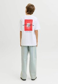 Hvid T-shirt med et rødt firkantet grafik på bagsiden, med sort tekst. Kombineret med lyseblå vidde bukser. Blødt bomuldsmateriale.