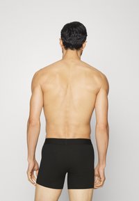Svarte boksershorts med en jevn tekstur og elastisk midjebånd, båret av en mannelig modell vist fra ryggen mot en nøytral bakgrunn.