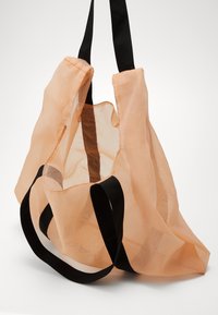 Translucent peach tote bag with black fabric straps. Lightweight material creates an open design, showcasing inner texture and structure.
