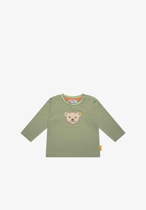 Chemise à manches longues vert clair pour tout-petit avec un écusson beige en forme de tête d'ours centré sur la poitrine et une étiquette orange sur la couture latérale.