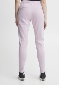 Ljusrosa sweatpants med elastisk midja, figurnära design och två bakfickor. Kombineras med svarta sneakers med hög skaft.