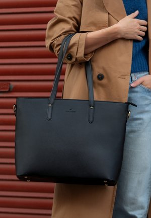 Zwarte tote bag van gestructureerd materiaal, met twee lange handgrepen, gouden hardware-accenten en een textuuroppervlak.