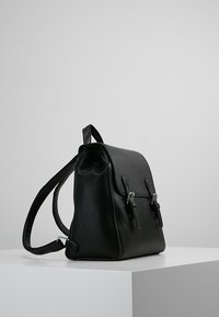 Mochila de cuero negro con forma estructurada, cuenta con herrajes plateados, dos hebillas frontales y correas ajustables. Textura suave en general.