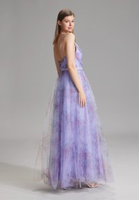 Bodenlanges Kleid aus durchscheinendem lavendelfarbenem Stoff mit Blumenmustern, dünnen Trägern und einem taillierten Oberteil. Transparente Überlagerung verleiht Textur und Tiefe.