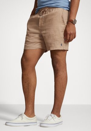 Beżowe lniane szorty z elastycznym paskiem i sznurkiem. Posiadają niebieskie logo na dolnym brzegu. W zestawie z białymi butami.