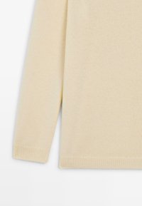 Pull léger beige avec un tissu tricoté texturé, des manches longues et des bords en côtes au niveau des poignets et de l'ourlet. Design simple sans motifs ni accents.