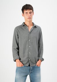 Camisa a cuadros grises con cuello, con botones en la parte delantera y mangas largas, combinada con jeans de mezclilla azul claro. El fondo es blanco liso.