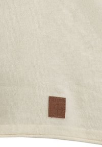 Jasno beżowy dziany szalik o teksturowanym wykończeniu z brązową skórzaną naszywką z logo w jednym rogu. Prosty design i miękki materiał.