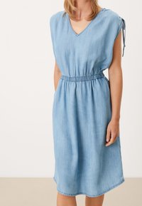 Ljust blå denimklänning med korta capesärmar, V-ringning, elastisk midja och fickor på båda sidor. Slät textur och knälång.