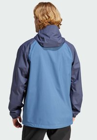 Chaqueta de hombre con cuerpo azul y mangas azul oscuro, cuenta con capucha, puños elásticos y una textura de tela suave.