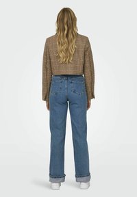 Veste brune cropped avec un tissage texturé, associée à un jean en denim bleu taille haute avec des revers et des poches arrière.