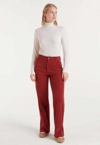 Pantalones de pana rojos con cintura alta, pierna recta y diseño de cinco bolsillos. La parte superior es un ajustado cuello de tortuga blanco de manga larga.