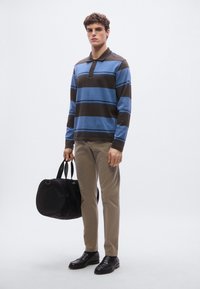 Μπλε και καφέ ριγέ πόλο με μακριά μανίκια, μπεζ παντελόνι, μαύρη τσάντα με χειρολαβές και μαύρα παπούτσια. Απλός, λειτουργικός σχεδιασμός.