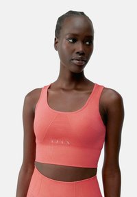 Koralesni sportski crop top izrađen od rebrastog materijala s okruglim izrezom, prilagođenim dizajnom i suptilnim logotipom duž rubova.
