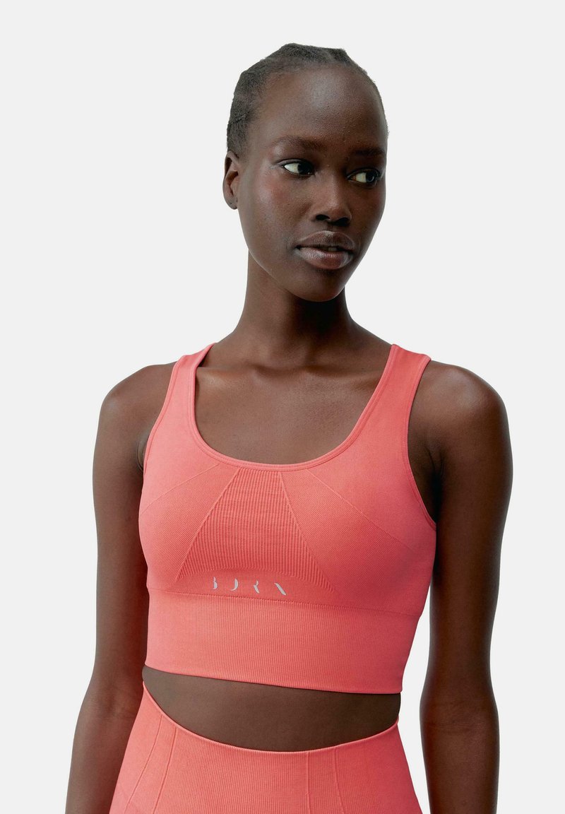 Koralesni sportski crop top izrađen od rebrastog materijala s okruglim izrezom, prilagođenim dizajnom i suptilnim logotipom duž rubova.