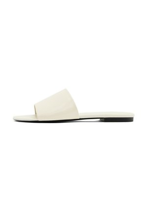 Nu-pieds plats avec une tige crème mate, un design à larges lanières, le bout ouvert et une semelle noire contrastante. Texture lisse dans l'ensemble.