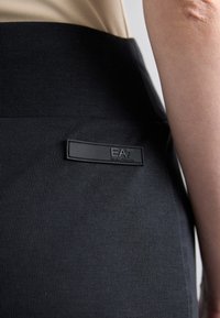 Zwarte geribbelde stofrok met een brede tailleband. Bevat een gemêleerd logo-label met de tekst "EA7" in een rechthoekig formaat.