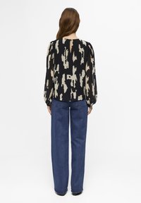 Blusa de estampado negro y crema con mangas abullonadas, detalle de abertura en la espalda, combinada con jeans de pierna ancha de cintura alta en azul.