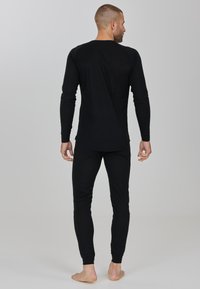 Haut thermique noir à manches longues et bas assortis en tissu doux et texturé, arborant un design ajusté et des poignets côtelés, vus de derrière.