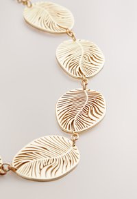 Gold-toned necklace featuring oval links with cut-out leaf patterns, showcasing a smooth texture and intricate design.