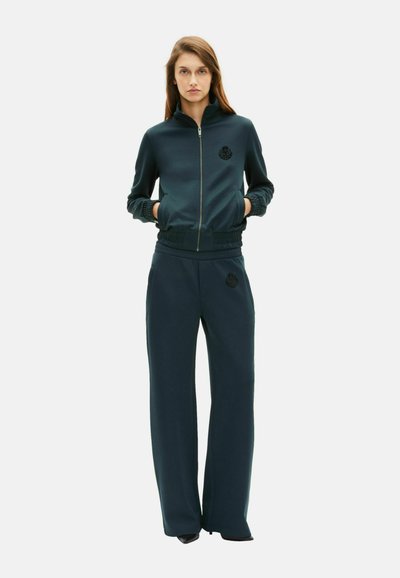 Marineblauw athleisure set bestaande uit een zip-up trainingsjack met een logo en een relaxed-fit broek met elastische taille, gemaakt van zachte, gladde stof.
