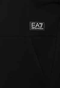 Felpa nera con tessuto a effetto, dotata di una grande tasca frontale e di una vistosa patch con il logo EA7 Emporio Armani.