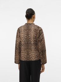 Leopard print jacket with long sleeves, smooth texture, rounded collar, and contrasting black trim. Worn over black trousers.