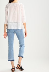 Vit långärmad topp med hålmönster, i kombination med ljusblå korta jeans med fransar och svarta platta sandaler.