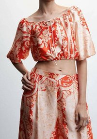 Rød og creme-mønstret crop top med puffærmer, der har en samlet halsudskæring og snøre, parret med en matchende nederdel.