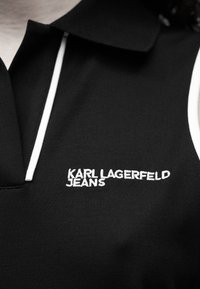Μαύρο πόλο με κλασικό γιακά, λευκή επένδυση και κεντημένο το λευκό λογότυπο "KARL LAGERFELD JEANS" στην αριστερή πλευρά.