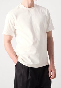 Katoenen T-shirt met ronde hals in off-white met korte mouwen; voorzien van subtiele "HUGO" logo op de borst; zachte textuur. Gecombineerd met zwarte broek.