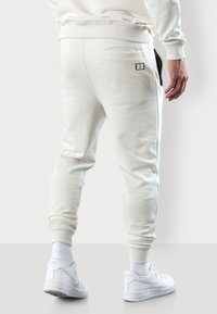Pantalons de jogging blancs en matériau doux, dotés d'une poche arrière, de poignets côtelés et d'un design minimaliste, associés à des baskets blanches.
