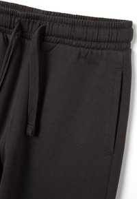 Dark gray sweatpants with a textured fabric, elastic waistband, drawstring, and side pockets. Features flat seams and minimal detailing.