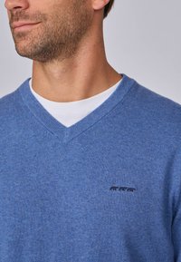 Pull bleu en v en tissu doux avec des bords côtes, arborant un petit logo bleu foncé de trois animaux sur la poitrine.