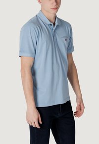 Polo shirt in cotone azzurro chiaro con colletto, patta a due bottoni e maniche corte. Presenta un logo ricamato e jeans in denim scuro.