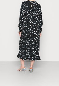 Černé šaty s modrými puntíky, dlouhými rukávy, volánkovým lemem a detaily s otvorem na zádech. Spárované s jasně modrými sandály na vysokém podpatku.