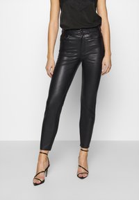 Svarta fuskläder slim-fit byxor med hög midja, med en slät yta och minimala sömnadsdetaljer. Bärs med svarta klackar med remmar.