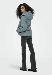 Chaqueta acolchada de color azul claro con capucha, presenta un diseño elegante y una textura suave. Combinada con jeans ajustados de color gris oscuro y botas negras hasta el tobillo.