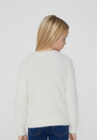 Weißer, flauschiger Pullover mit rundem Halsausschnitt und langen Ärmeln, kombiniert mit blauen Jeans; weiche Textur und schlichtes Design, ohne Muster oder Akzente.