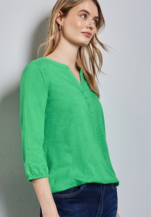 Grön, långärmad blus med V-ringning, som har tre knappar vid halsringningen och elastiska manschetter. Mjuk, texturerad tyg.