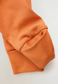 Tissu orange côtelé, avec une texture douce et des manches à revers. Le design met en avant une silhouette ajustée et une finition lisse.