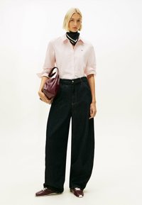 Camisa de rayas rosa claro, vaqueros anchos de pierna oscura, bufanda en blanco y negro, bolso burdeos y zapatillas oscuras con detalles blancos.