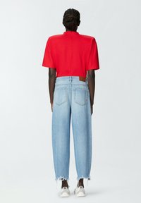 Top rosso a maniche corte con collo alto, abbinato a jeans a gamba larga azzurri chiari con orli strappati e una patch in pelle marrone sul retro.