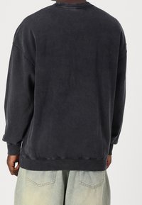 Sudadera negra de corte amplio con cuello y puños acanalados. Fabricada con una tela suave, presenta una textura lisa y un diseño minimalista.
