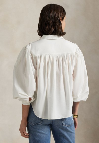 Hvit bluse med pufferm og detaljer i ryggen samt krage. Mykt stoff, løs passform og mansjetter med knapper. Brukt med blå jeans.