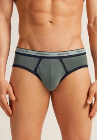 Herrenunterwäsche in einem gedämpften grünen Stoff mit navyfarbenen Akzenten. Verfügt über einen kontrastierenden Bund mit Markenlogo, körpernahen Schnitt und glatter Textur.
