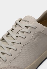 Λευκά δερμάτινα αθλητικά παπούτσια με υφασμάτινες επιφάνειες, στρογγυλεμένη μύτη, επίπεδα κορδόνια, διακριτικό λογότυπο και λεπτομέρειες σε πιο ανοιχτό μπεζ στο πέλμα.